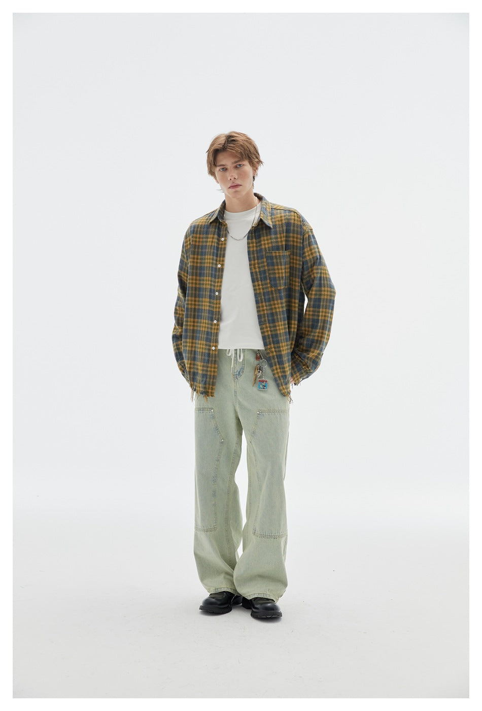 Full-length front view of a model wearing a dark blue and mustard plaid shirt over a white tee with pale green pants.