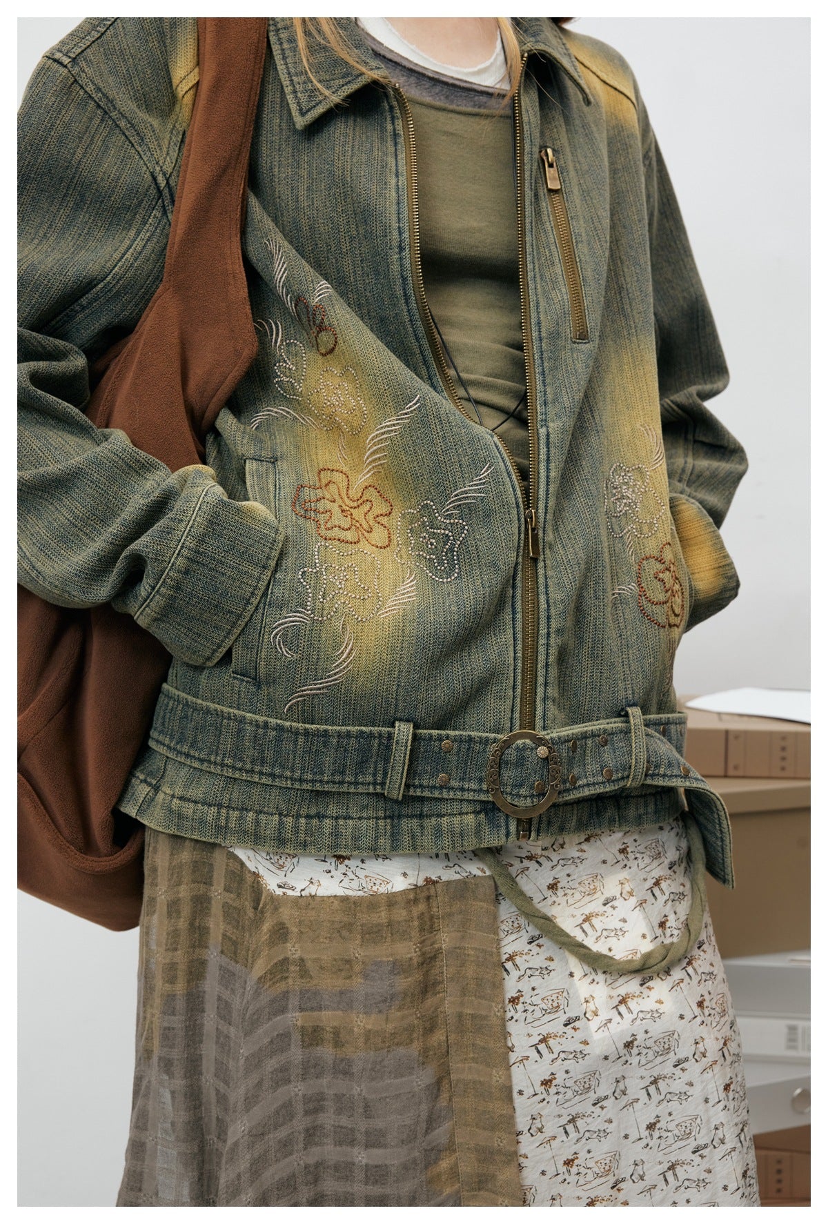 Close-up of the olive jacket’s floral embroidery, zip pockets, front zipper, and buckle belt hem.