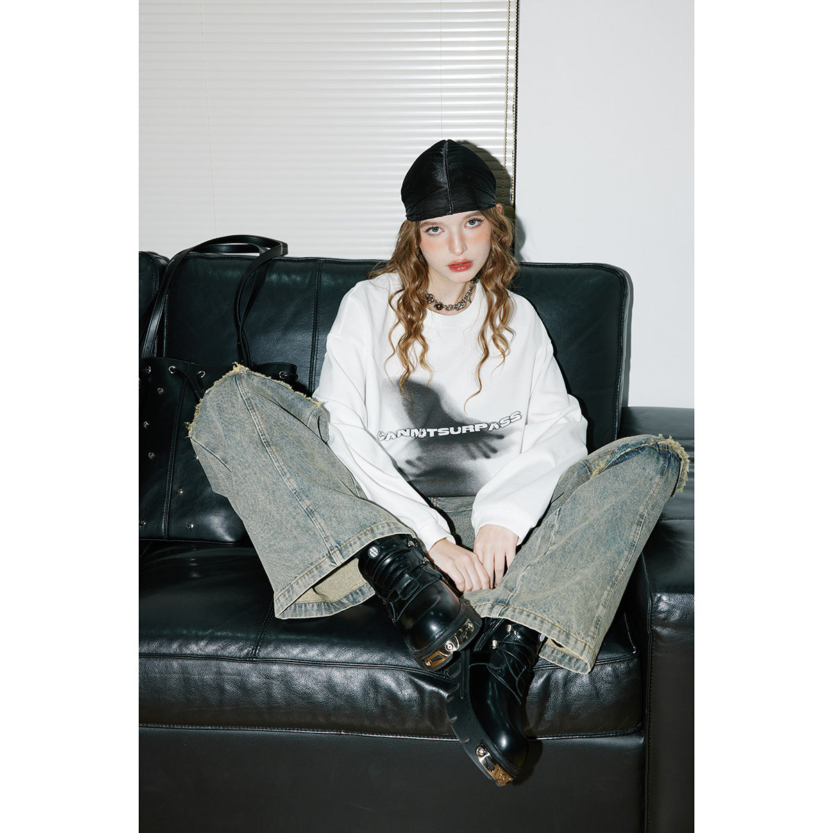 Model seated in a white oversized graphic sweatshirt with a dark front print.