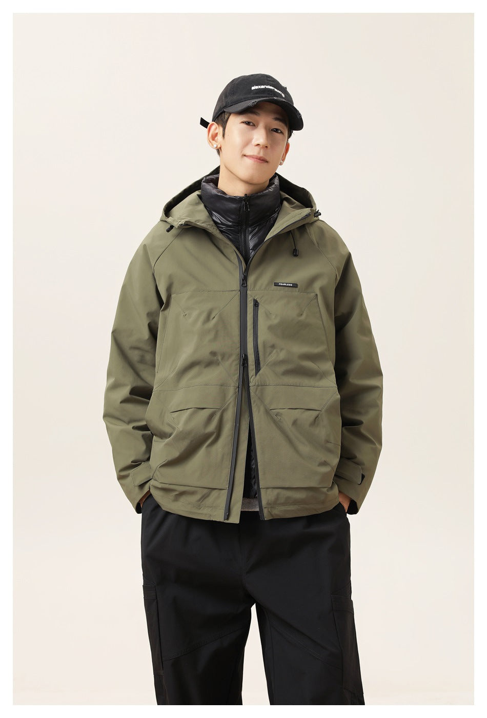 Model wearing an olive hooded jacket with a front zipper, chest zip pocket and large lower pockets.