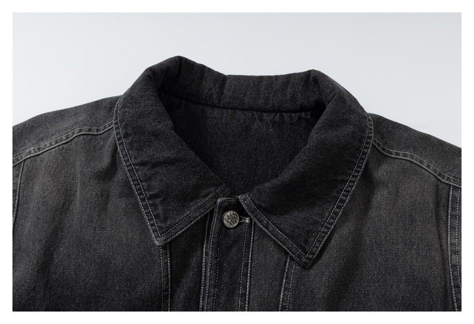 Close-up of a black denim jacket's pointed collar, top button and contrast stitching.