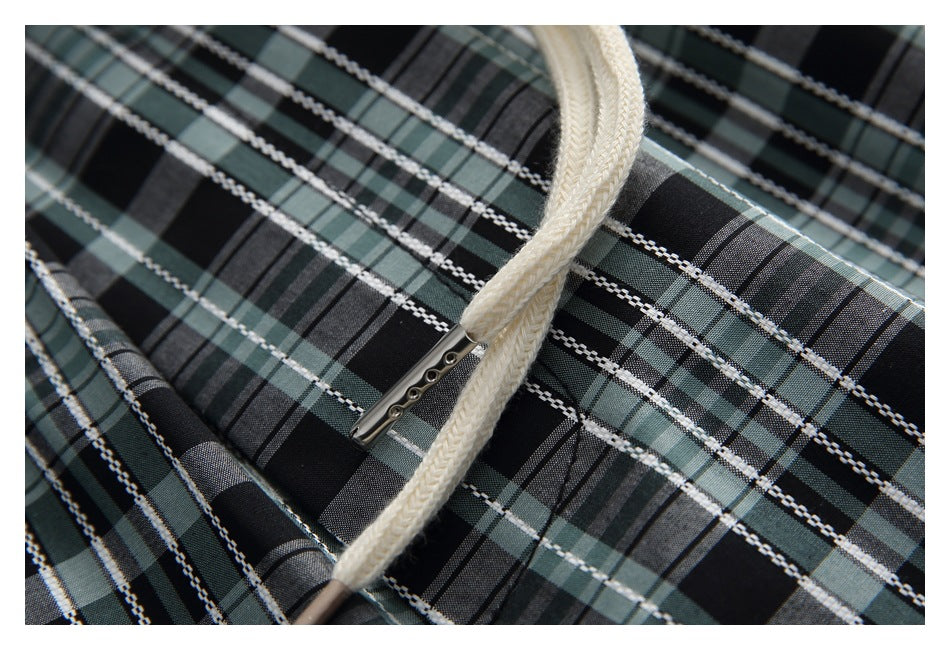 Cream drawstring with metal tips lies over black, gray, and muted green plaid fabric.