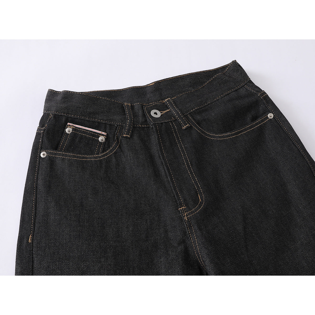 Close-up of black jeans' front waistband, button, fly, pockets, and tan contrast stitching.