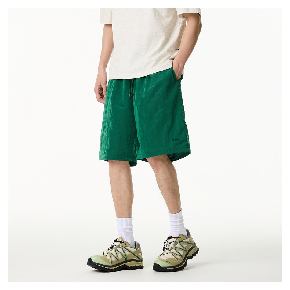 Model wearing green relaxed shorts with hand in side pocket, three-quarter side view with sneakers