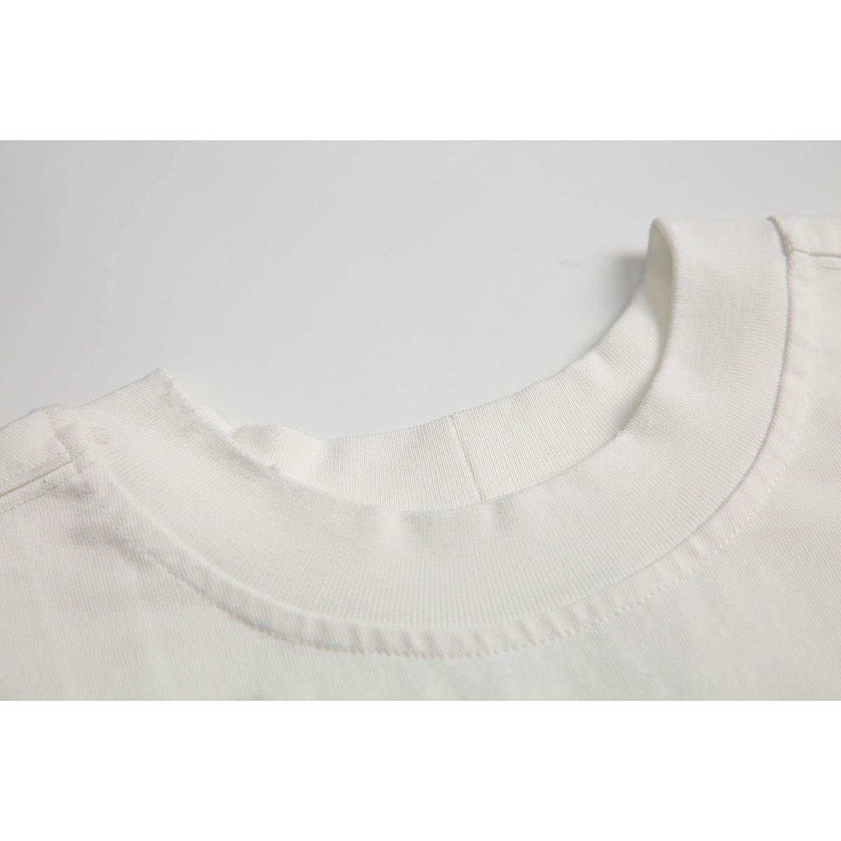 Close-up of an off-white T-shirt's ribbed crew neckline and shoulder seam.
