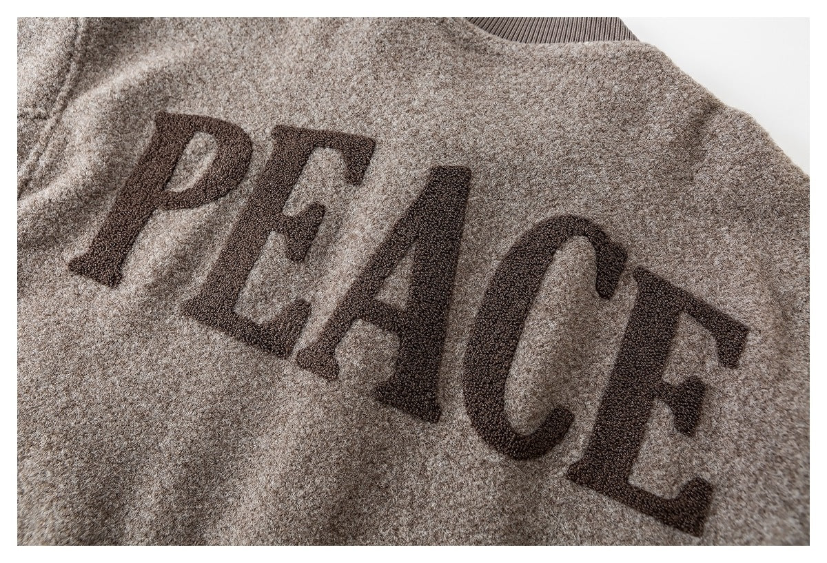 Close-up of the word “PEACE” in dark lettering on a beige knit garment.