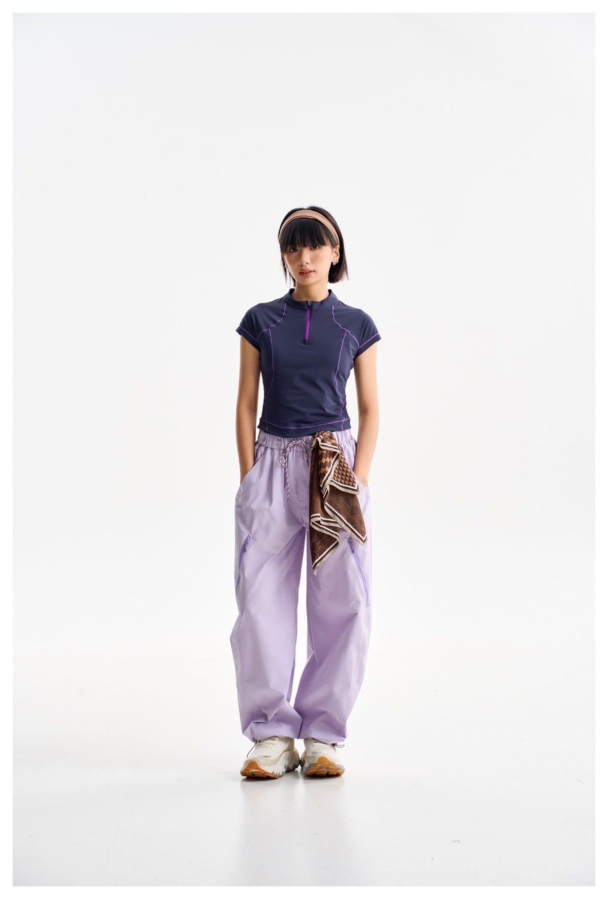 Model wearing a navy short-sleeve zip-neck top with purple piping and loose lavender pants.