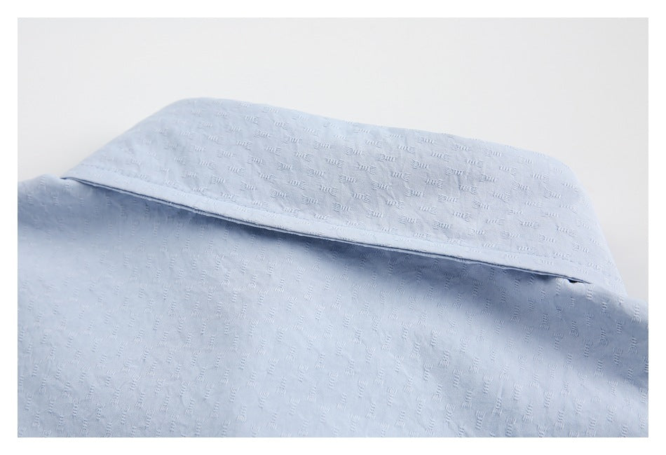 Close-up of a pale blue shirt collar with a subtle raised repeating pattern.