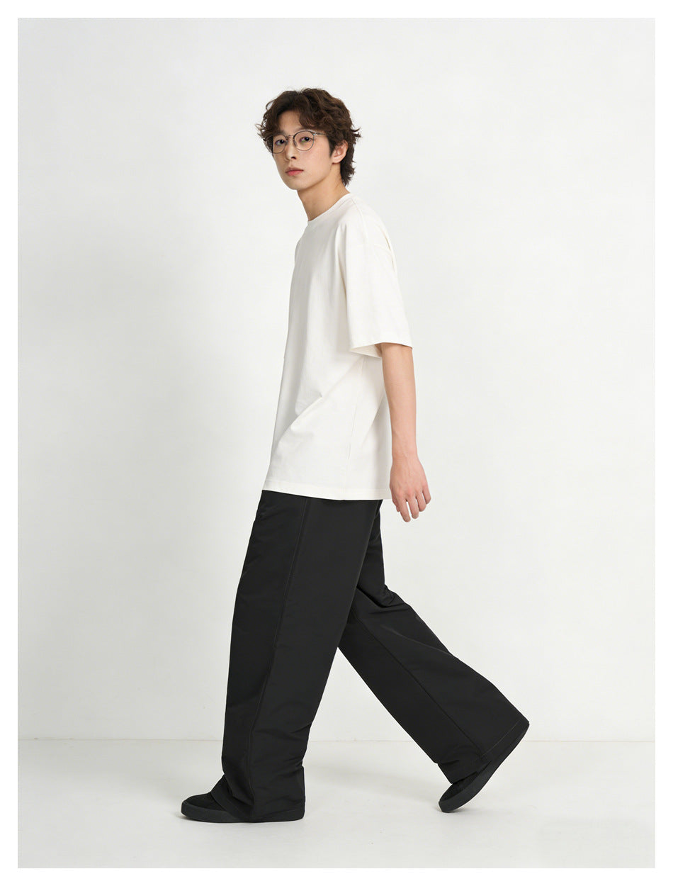 Side view of a model walking in a white oversized T-shirt and loose black trousers.