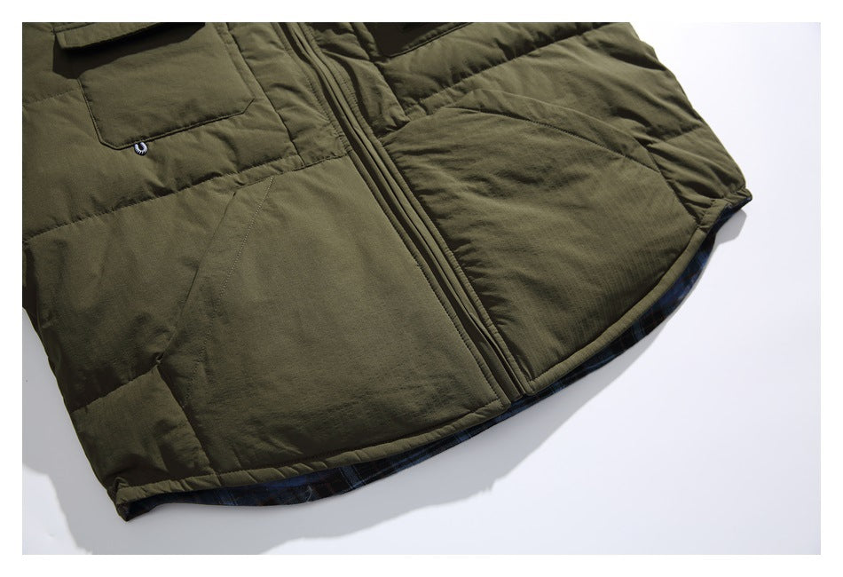 Partial view of an olive green jacket front with pockets, a central zipper, and dark plaid lining at the hem.