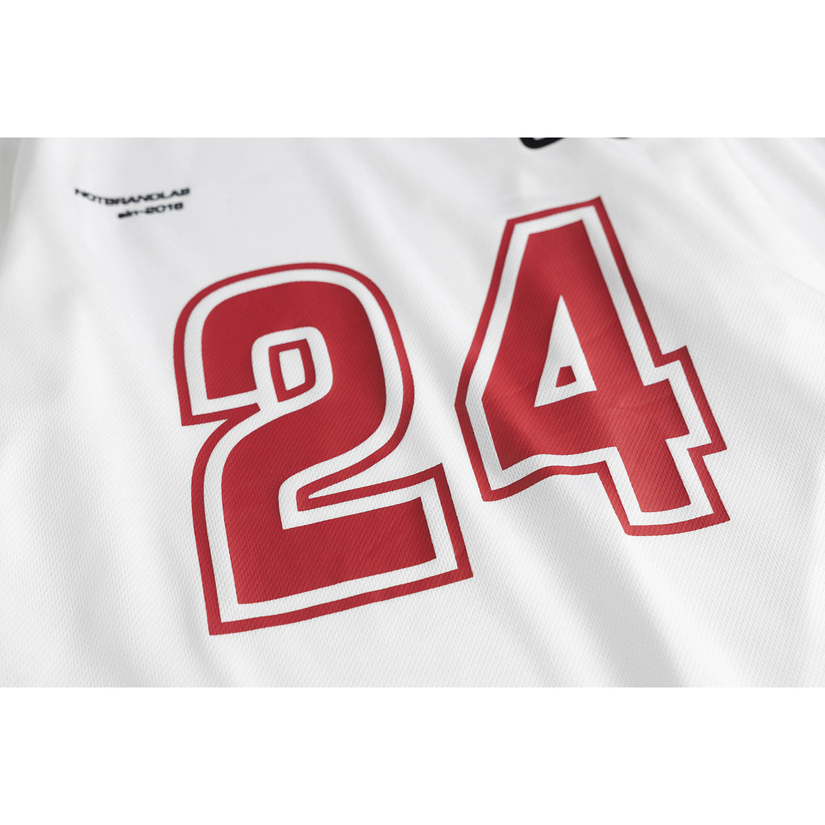 Close-up of a white jersey showing a large red outlined number 24 and small black chest text.