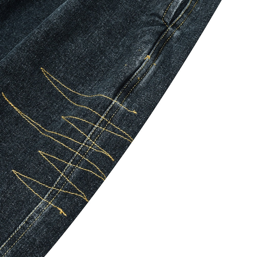 Close-up of dark denim leg seam with decorative, angular golden-yellow stitching.