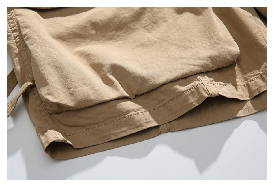 Close-up of tan shorts showing a stitched hem, folded fabric, and a drawstring at the left edge.