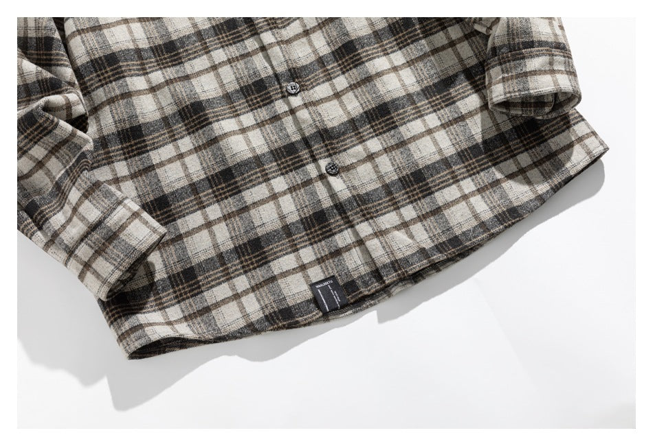 Cropped view of the plaid shirt's buttoned front, hem, and cuffs on a white background.