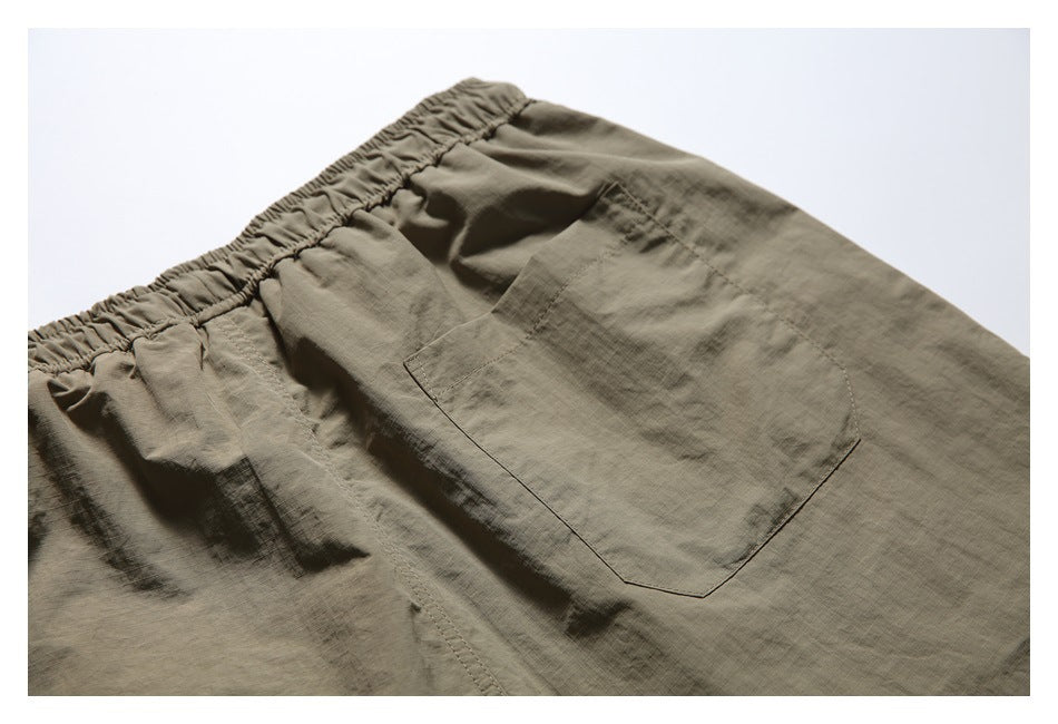 Close-up of olive-khaki shorts showing the gathered elastic waistband and a large stitched pocket.