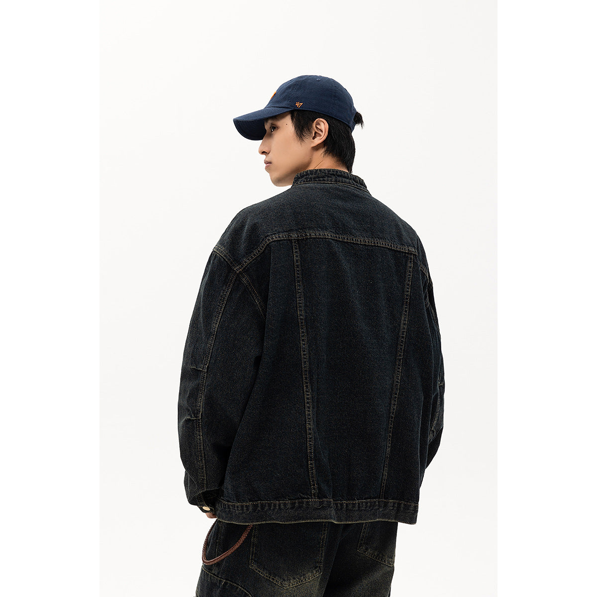 Back view of a model wearing an oversized black washed-denim jacket with panel seams.