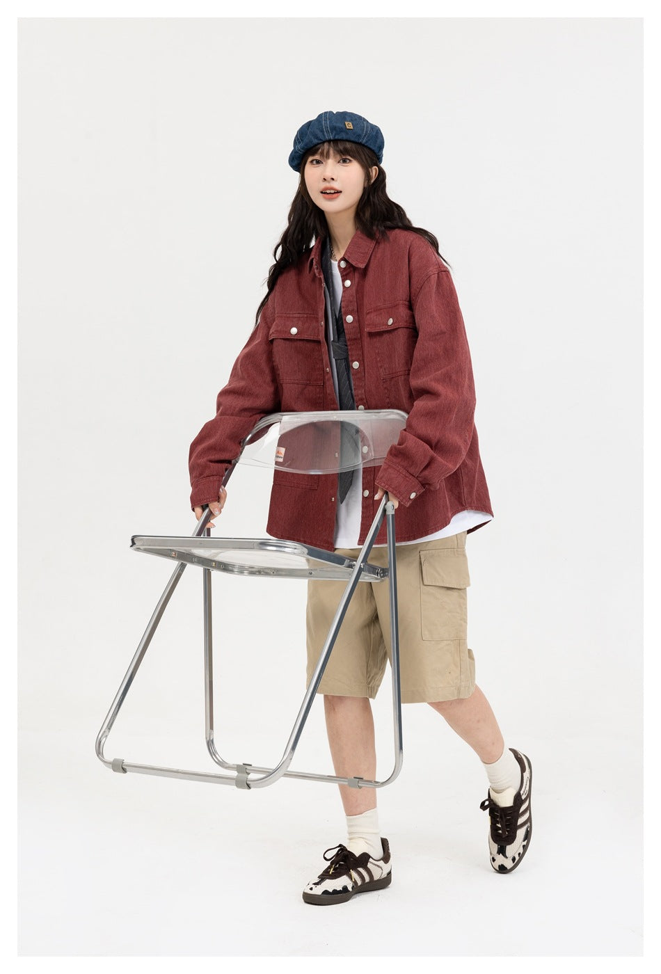 Model wearing a muted red button-front utility overshirt with large pockets, beige cargo shorts and a blue cap.