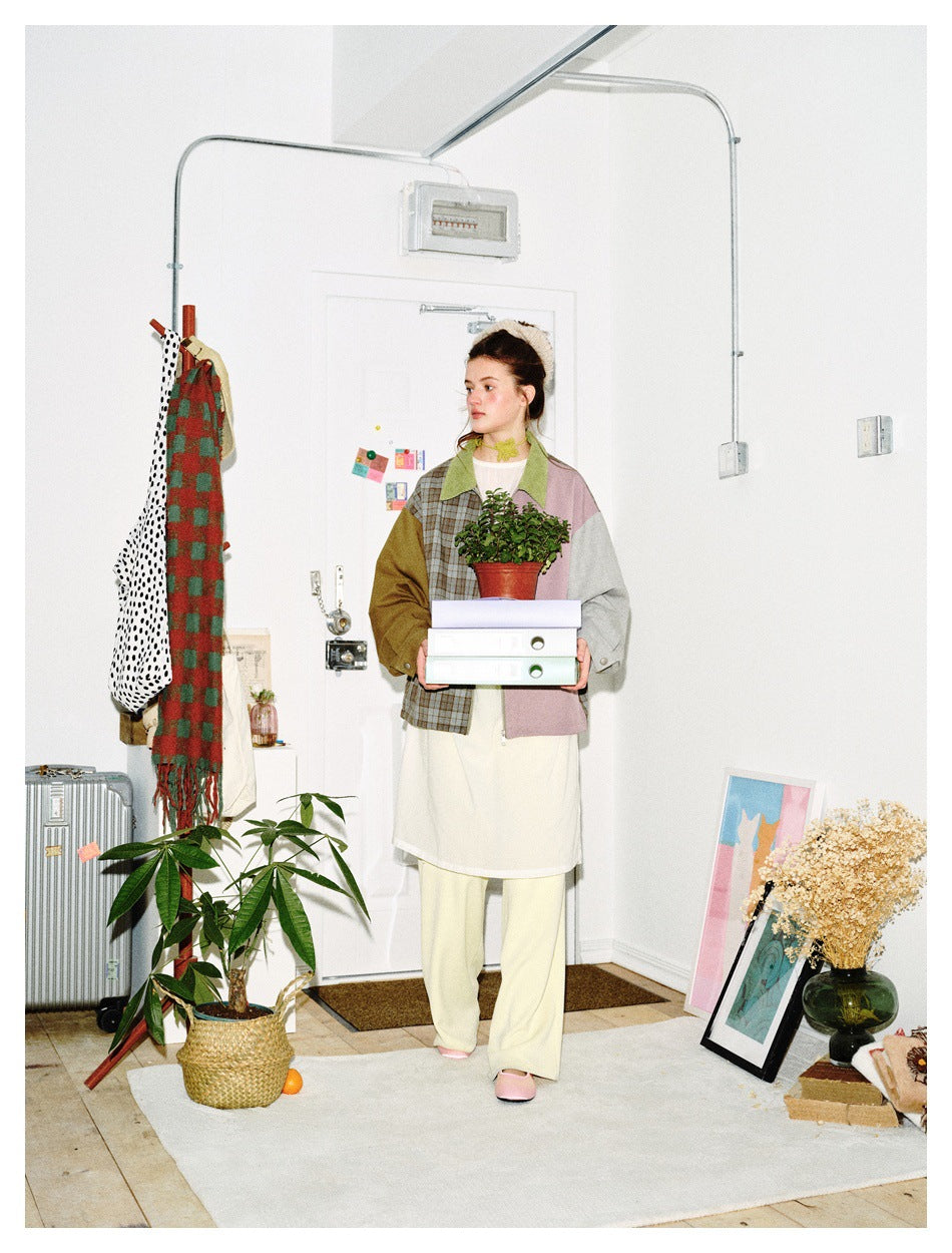 Front view of a model in a color-block jacket with a plaid panel, green collar, mauve panel, and contrasting sleeves.