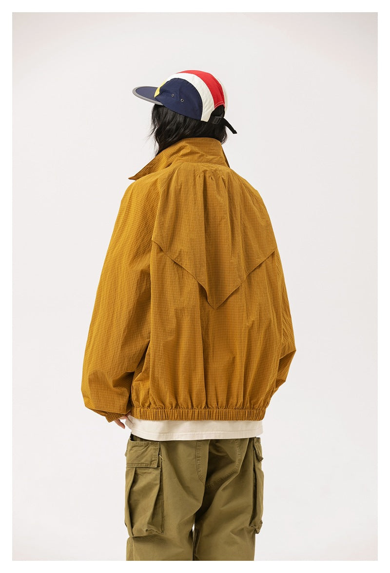 Rear view of a model wearing a mustard-gold jacket with a cape-like back yoke and elastic hem.