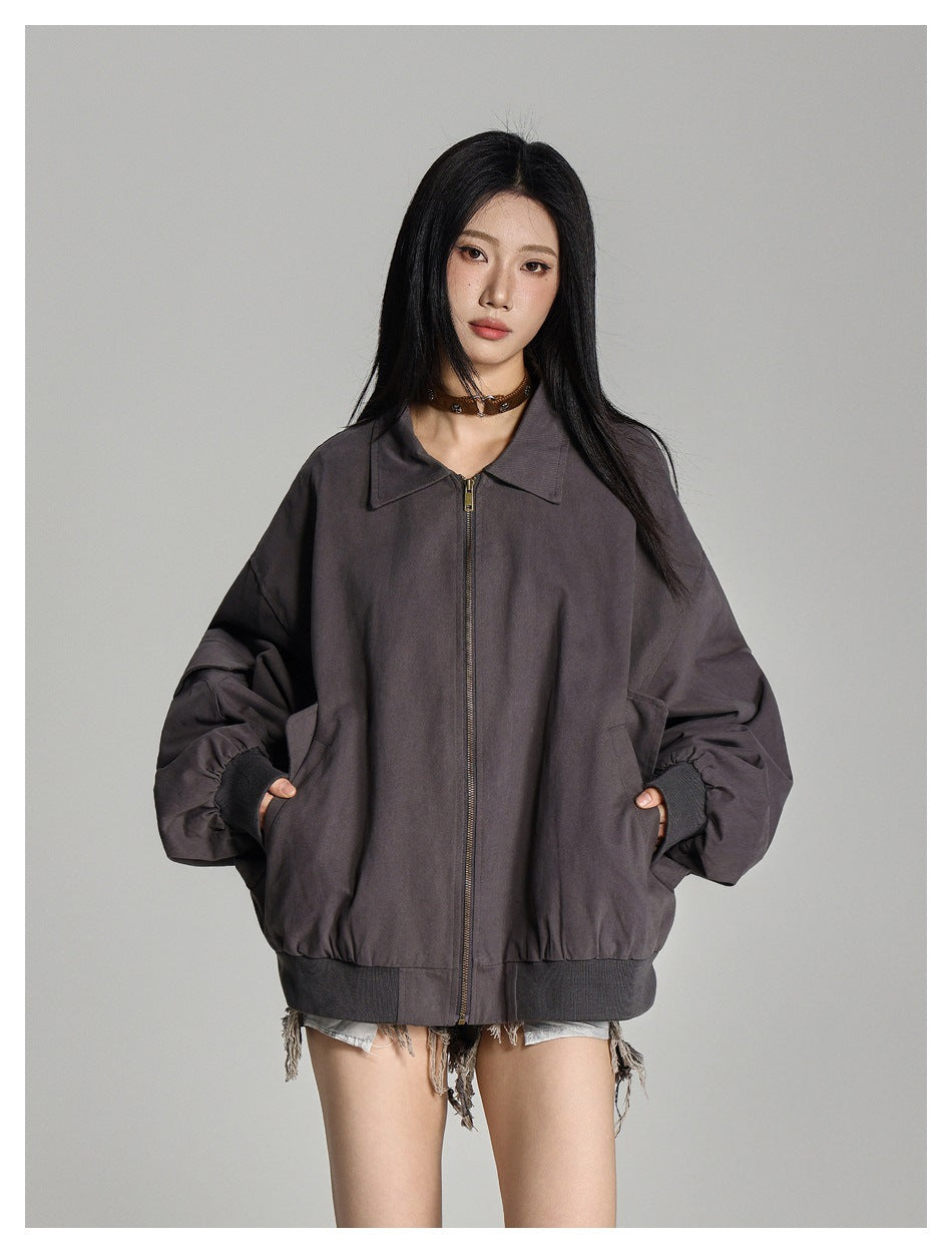 Front view of a model wearing a charcoal-gray oversized zip jacket with a pointed collar, large pockets, and ribbed cuffs and