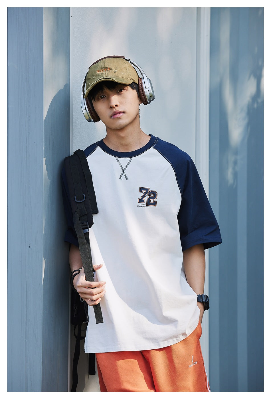Model wearing a white raglan T-shirt with navy sleeves, crossed neckline stitching and a 72 chest graphic.