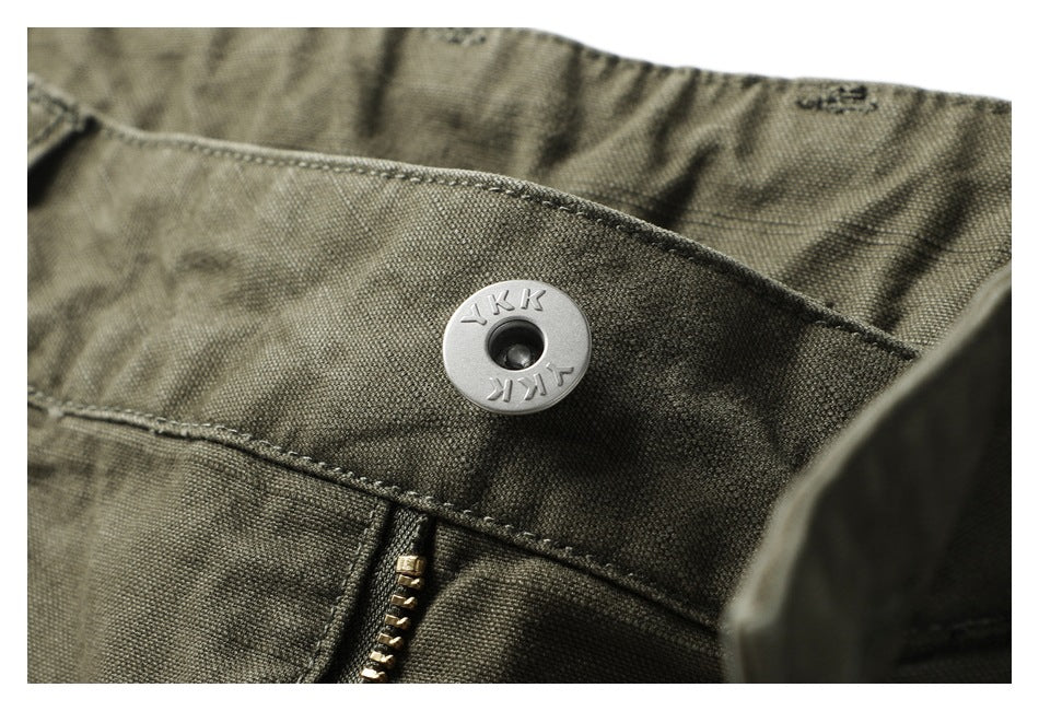 Close-up of an olive pants waistband snap and brass-colored zipper; the snap is marked YKK.