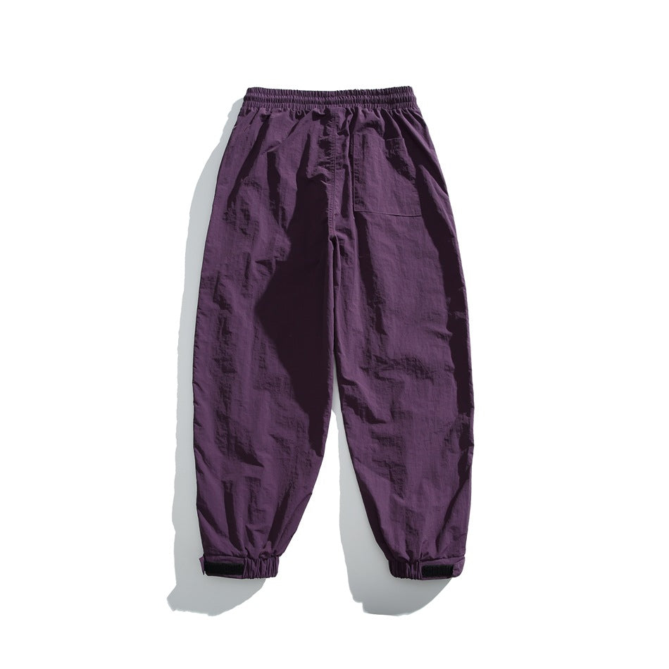 Back view of purple loose-fit pants with an elastic waist, single patch pocket, and elastic cuffs.