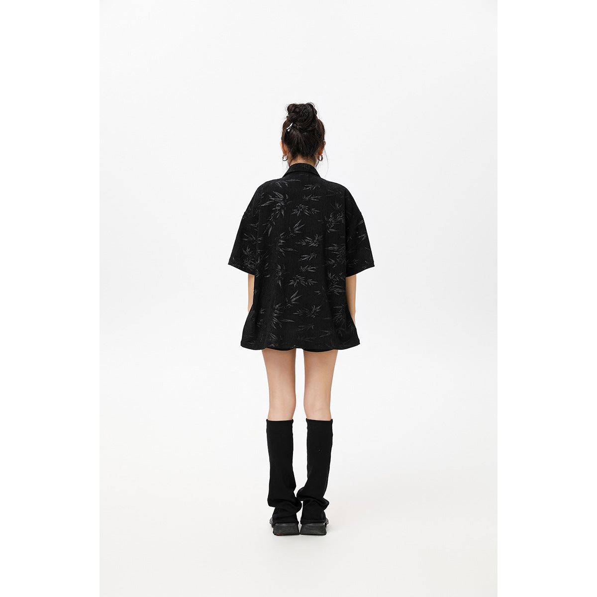 Back view of a model wearing a loose black short-sleeve shirt with a subtle leaf pattern.