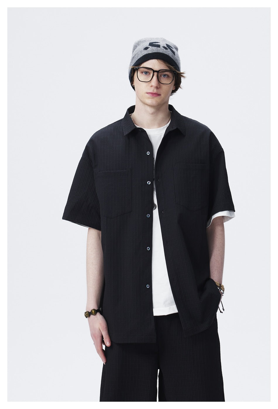 Front view of a model wearing a black short-sleeve button-up shirt over a white T-shirt.