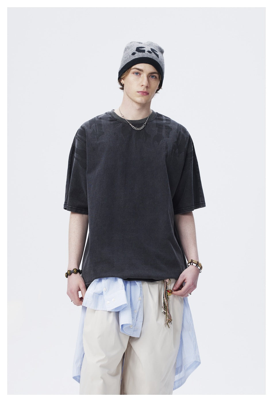 Model wearing an oversized charcoal T-shirt with subtle tonal graphics across the shoulders; upper body shown.