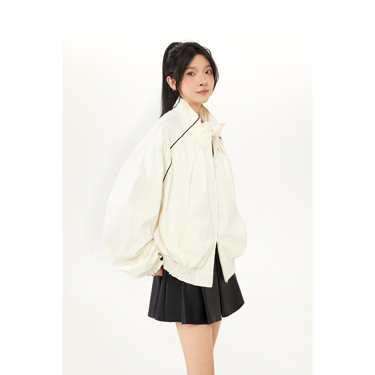 Three-quarter view of a model wearing an ivory oversized jacket with black piping and a black flared skirt.