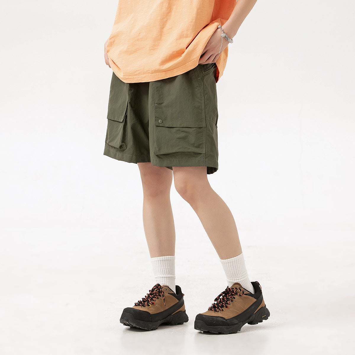 Cropped model wearing olive cargo shorts with large flap pockets, paired with an orange shirt and hiking shoes.