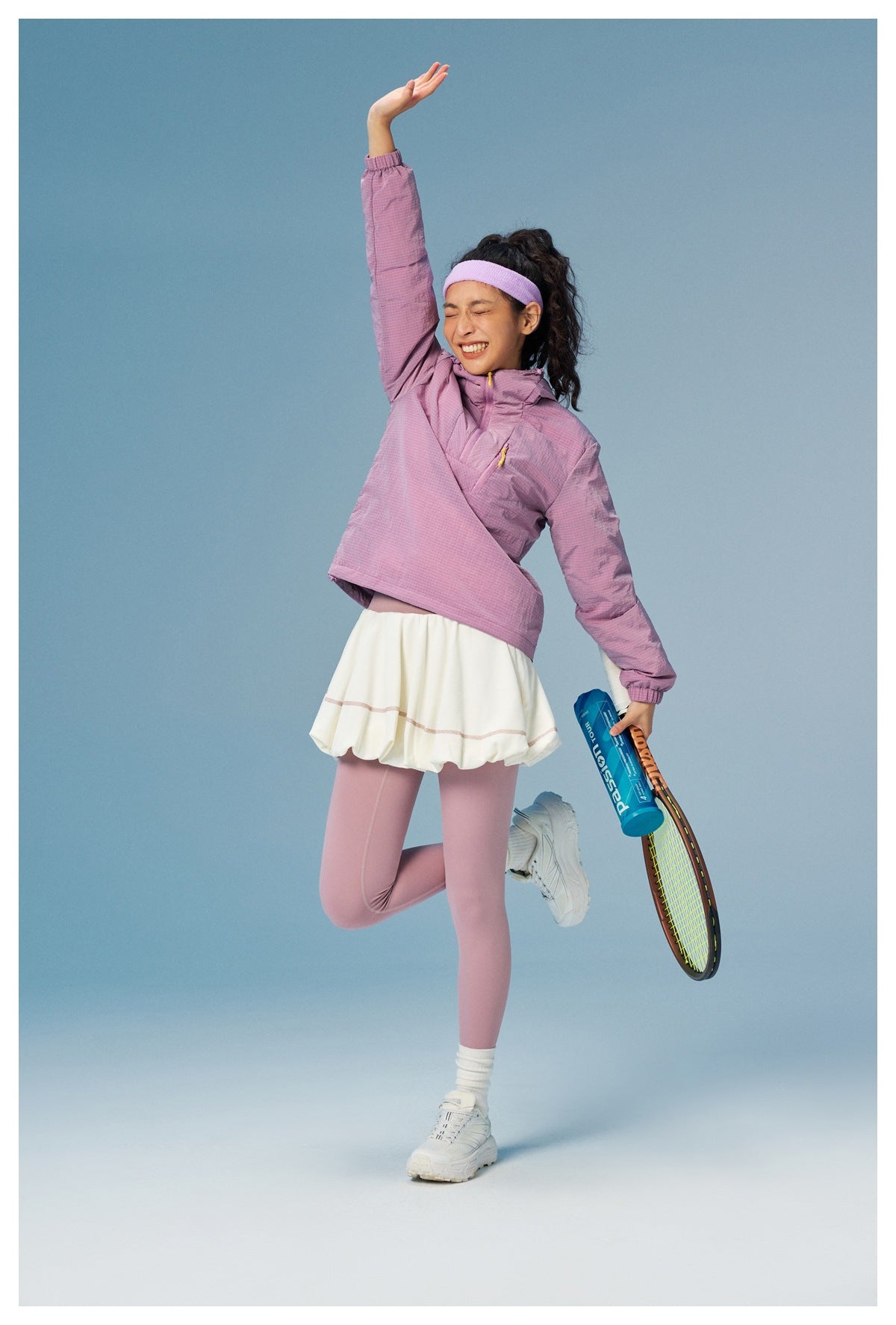 Model in a lilac hooded pullover and matching leggings, posing with a tennis racket.