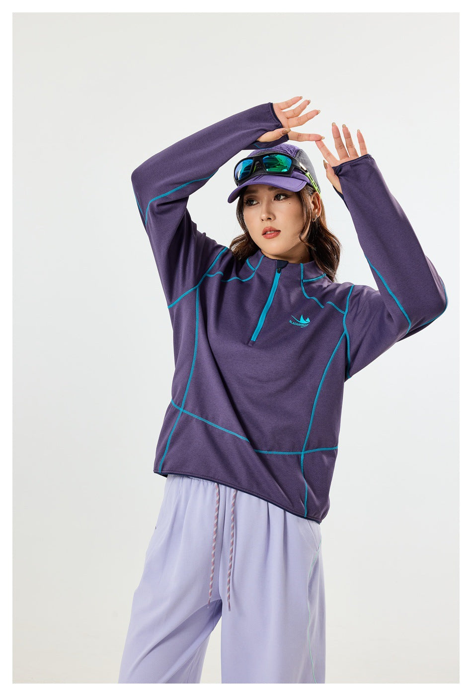 Model wearing a purple quarter-zip top with turquoise seams, shown from the front with arms raised.