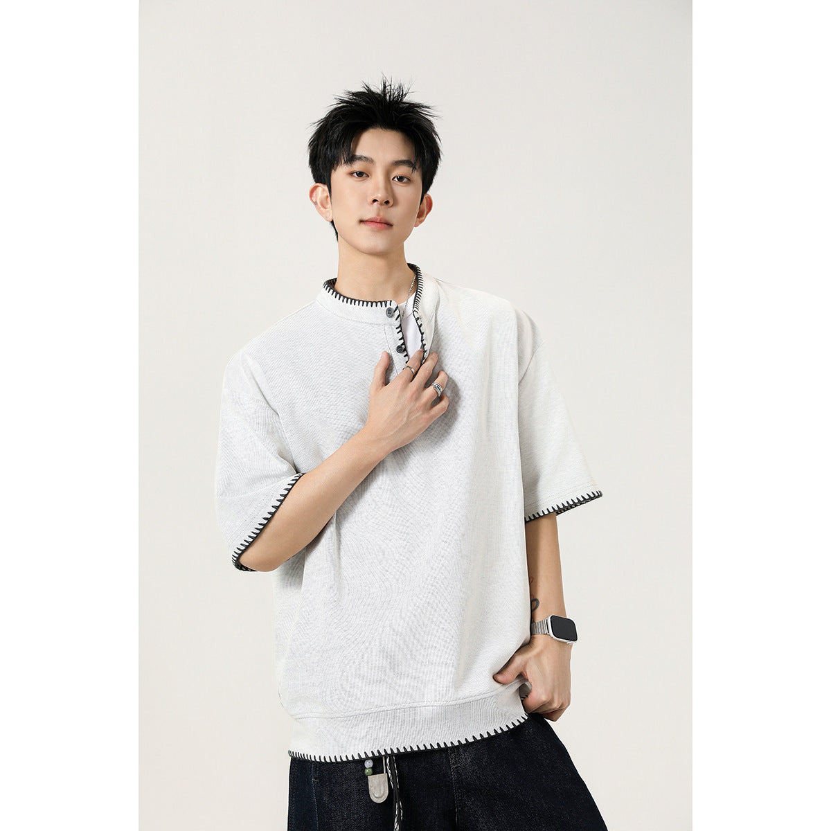 Close view of an off-white short-sleeve henley with dark contrast stitching around the collar, placket, cuffs and hem.