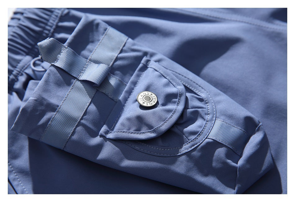 Close-up of a blue shorts cargo pocket with fabric straps, a curved snap flap, and visible stitching.