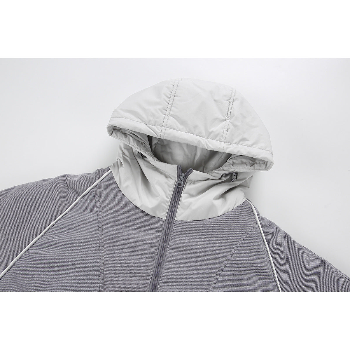 Close-up of a gray jacket with a light gray hood, center zipper, and white piping.