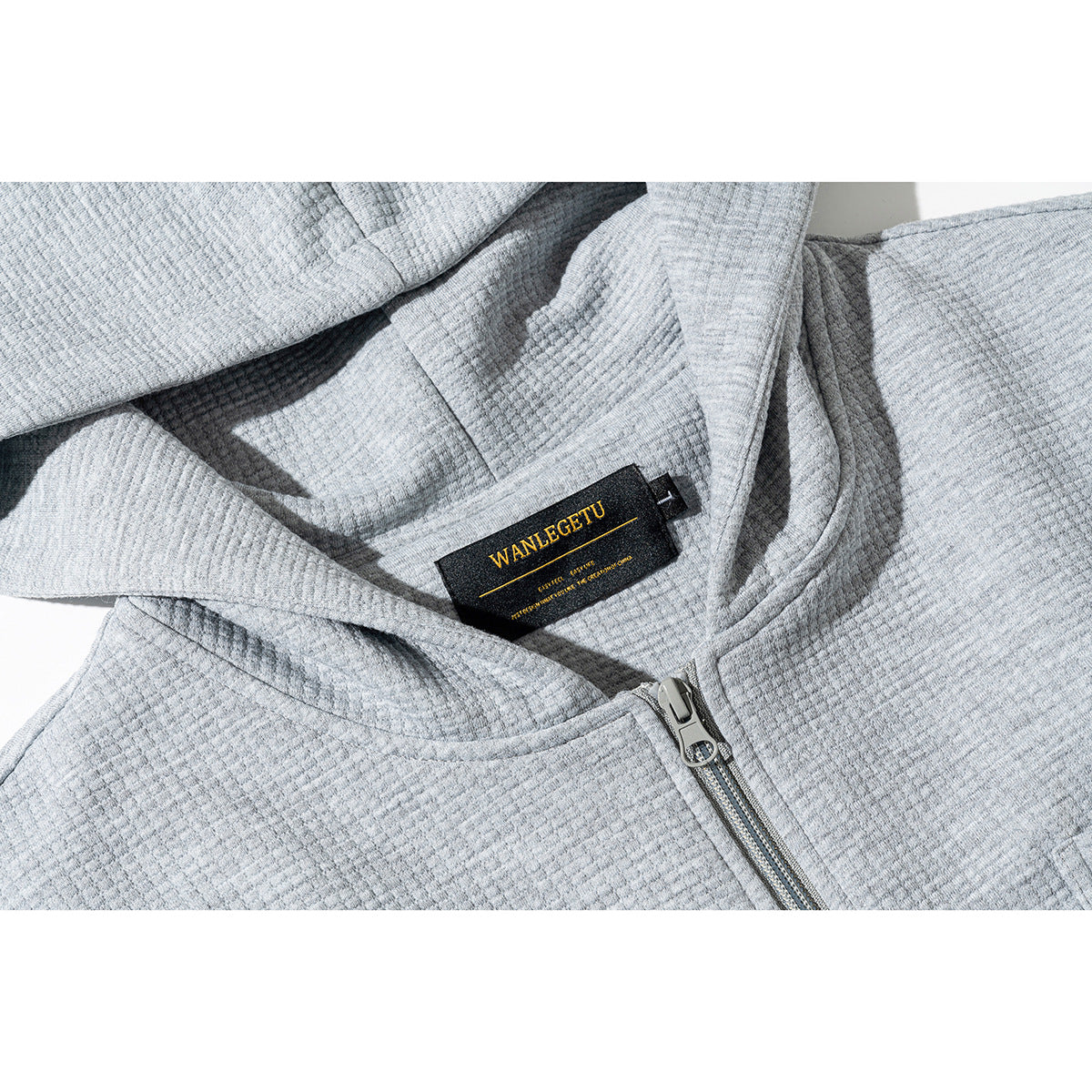 Close-up of a light gray hooded zip jacket showing its hood, zipper, textured fabric, and black neck label.