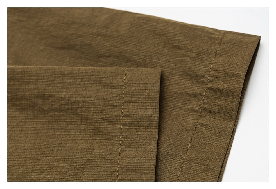 Close-up of olive-brown fabric showing overlapping folded edges and parallel stitched hems.