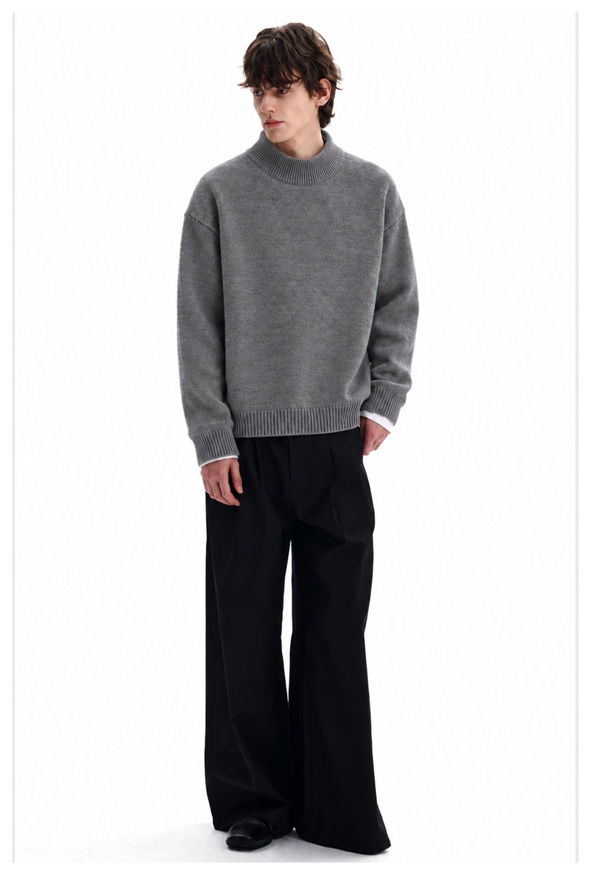 Full-length view of a man wearing a gray high-neck sweater with black wide-leg trousers.