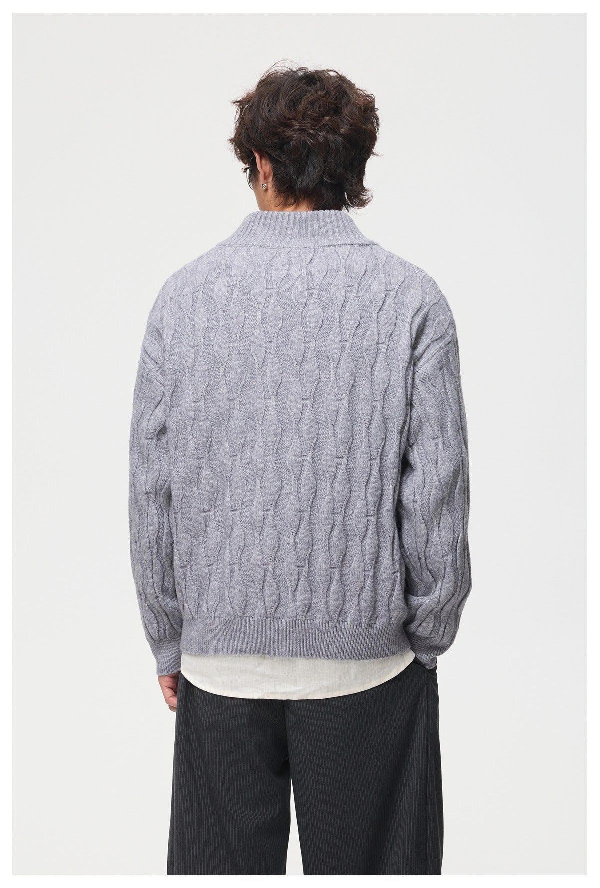 Back view of a model wearing a light gray cable-pattern sweater with ribbed collar and hem.