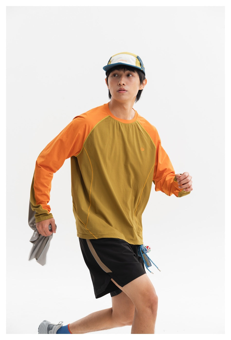 Action pose showing a model in an olive top with orange sleeves and black shorts.