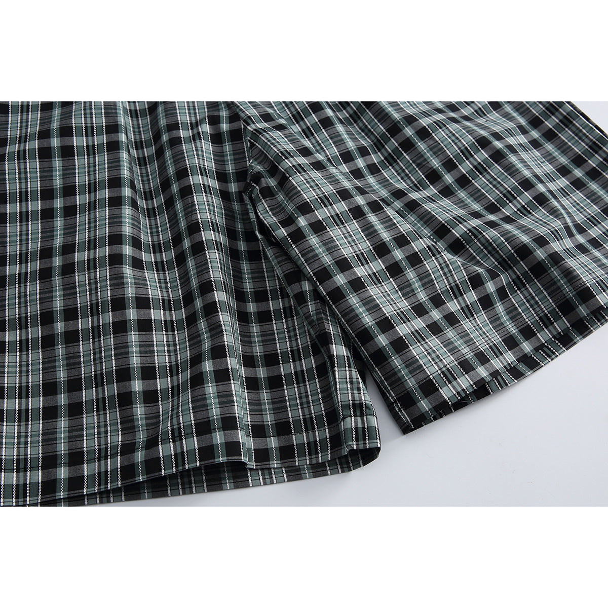 Close-up of the legs and hems of black, gray, and muted green plaid shorts.