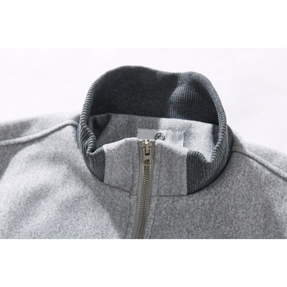 Close-up of a light gray zip jacket's dark ribbed stand collar and front zipper.