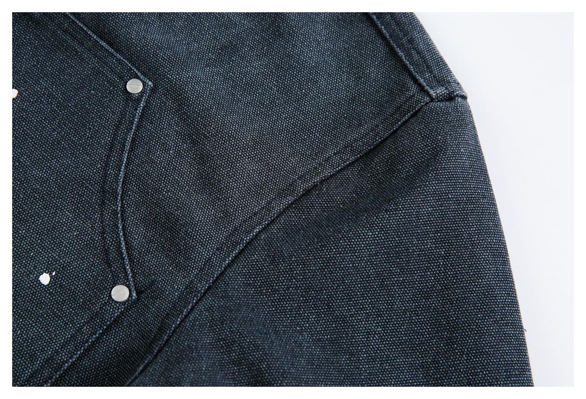 Close-up of dark textured denim showing a curved snap pocket edge and stitched garment panels.