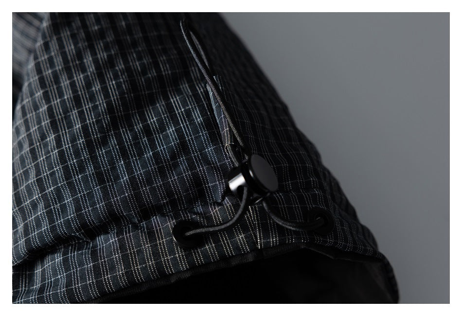 Close-up of a black cord lock and drawcord on a dark plaid garment.