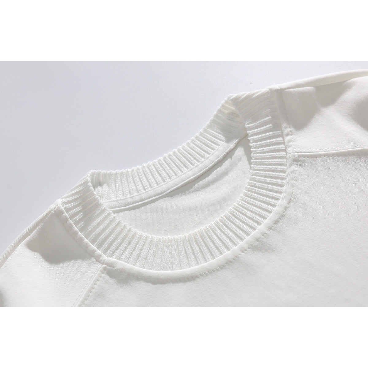 Close-up of a white T-shirt with a wide ribbed crew neckline and shoulder stitching.