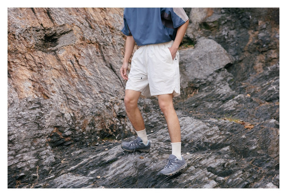 Cropped model posing on rocks in white elastic-waist shorts with a blue top.