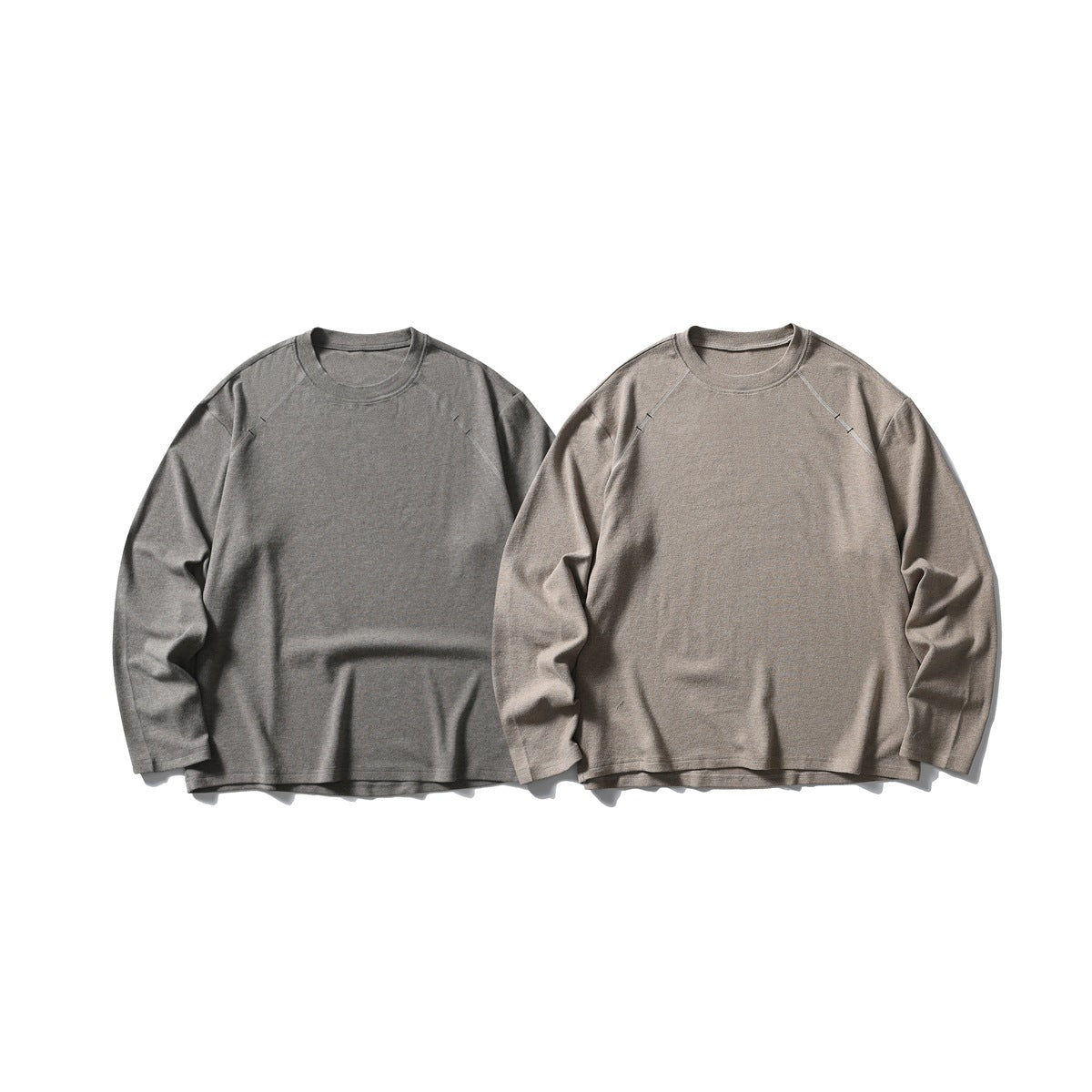 Two long-sleeve raglan crewneck sweatshirts shown from the front in charcoal gray and taupe.