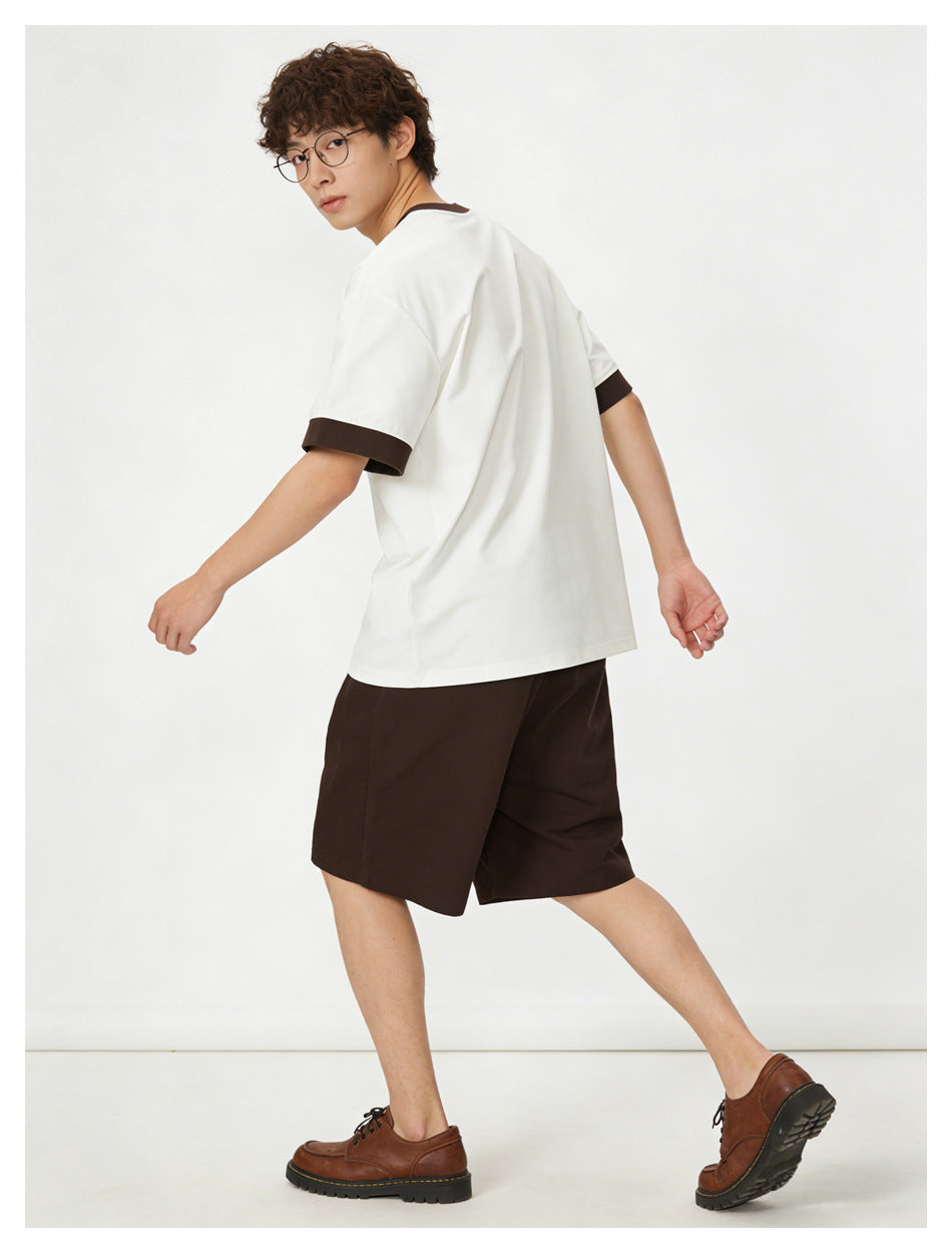 Model turned to show the back of a white T-shirt with dark brown collar and sleeve cuffs, paired with dark brown shorts.